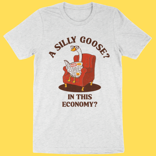 Heather gray t-shirt featuring a cartoon goose in a red armchair reading a newspaper with text 'A Silly Goose? In This