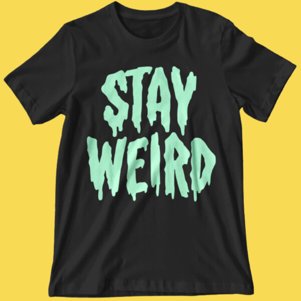 Black graphic tee with glow-in-the-dark mint text reading 'Stay Weird' in dripping horror style font on yellow background