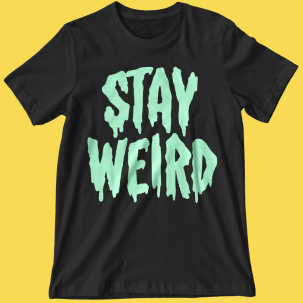 Black graphic tee with glow-in-the-dark mint text reading 'Stay Weird' in dripping horror style font on yellow background