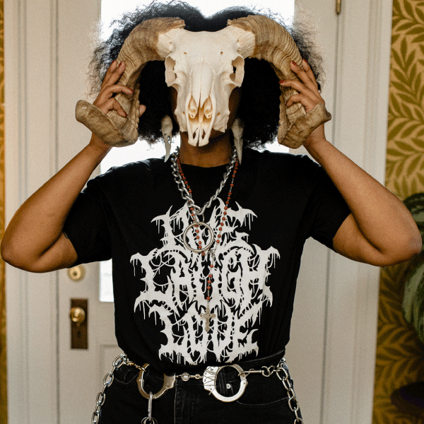 Black graphic tee with inverted pentagram design and 'Live Laugh Love' text, modeled with horned skull mask indoors.