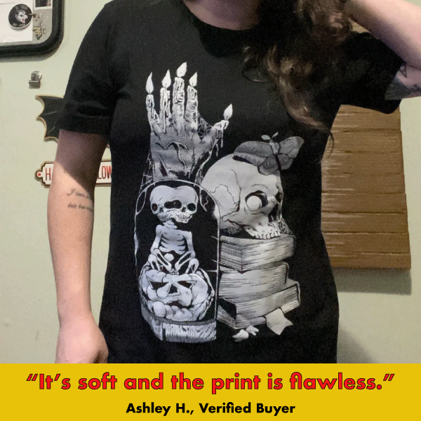 Black graphic tee featuring spooky stacked skulls, candles, and books with 'Oddities' theme in gothic style.