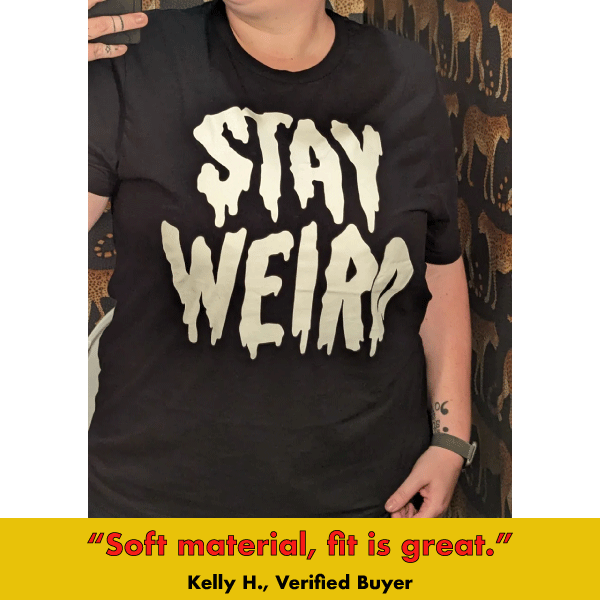 Black graphic tee with glow-in-the-dark 'Stay Weird' text in distressed font style on dark background
