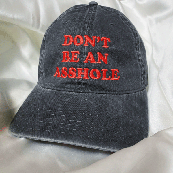 A charcoal grey, mineral wash unstructured baseball cap with red embroidery with text that reads don't be an asshole