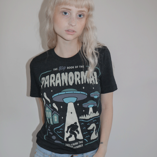 Black graphic tee featuring UFO and paranormal imagery with 'The Big Book of the Paranormal' text in blue and white on black.