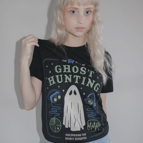 Woman wearing graphic tee that reads: the big book of ghost hunting, discovering the dearly departed with icons featuring a ghost and ghosthunting equipment